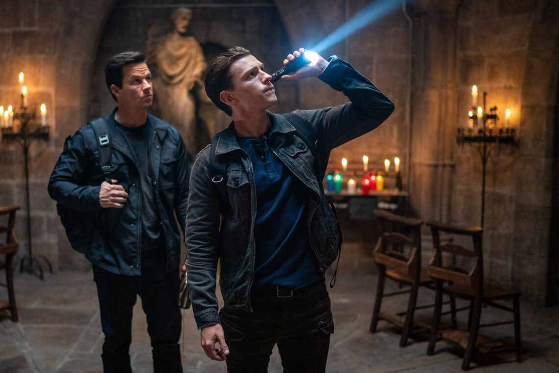 Nathan Drake (gespielt von Tom Holland) und Victor Sullivan (gespielt von Marc Wahlberg) untersuchen einen Kircheninnenraum mit einer Taschenlampe nach Hinweisen