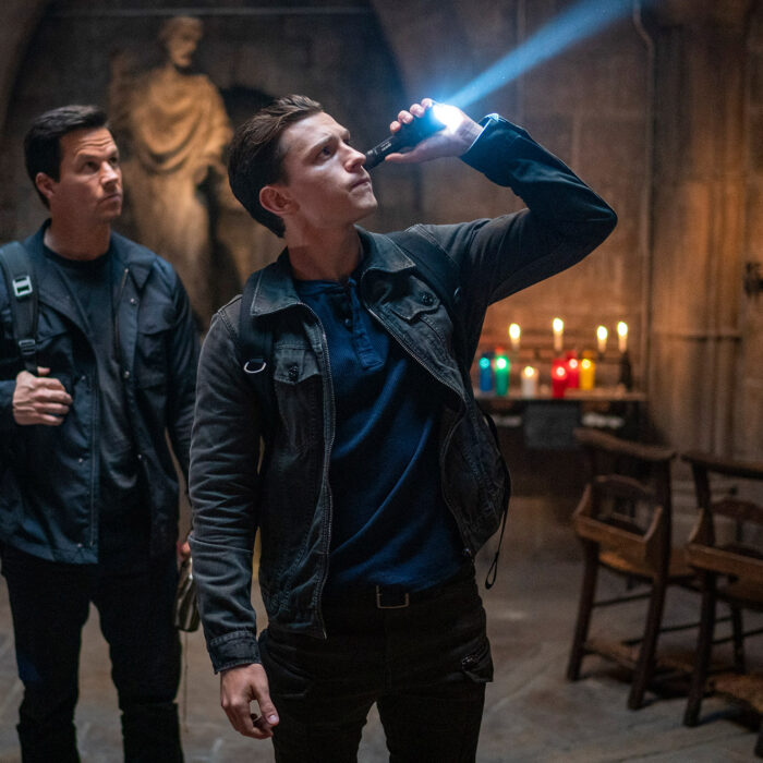 Nathan Drake (gespielt von Tom Holland) und Victor Sullivan (gespielt von Marc Wahlberg) untersuchen einen Kircheninnenraum mit einer Taschenlampe nach Hinweisen