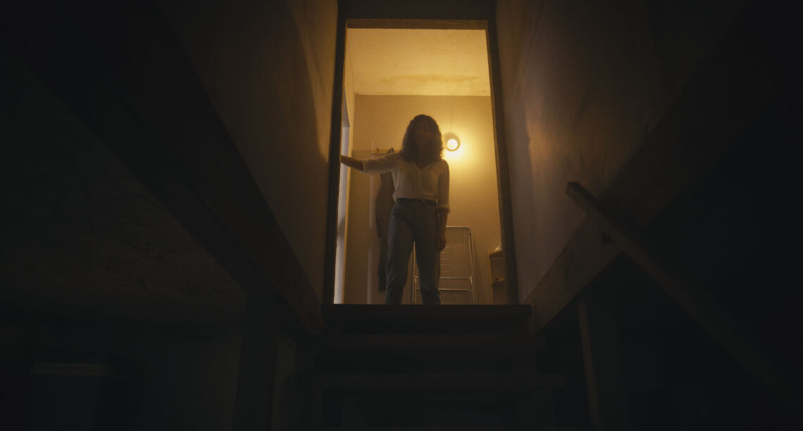 Eine Frau steht an der Tür zu einer dunklen Kellertreppe und schaut hinunter