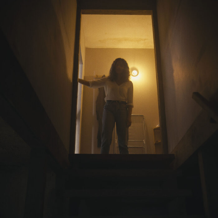 Eine Frau steht an der Tür zu einer dunklen Kellertreppe und schaut hinunter