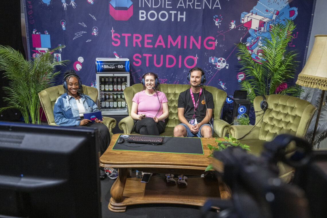 Foto vom Indie Arena Booth Streaming Studio in dem 3 Personen auf einer Couch sitzen und spielen. Foto: Koelnmesse / gamescom