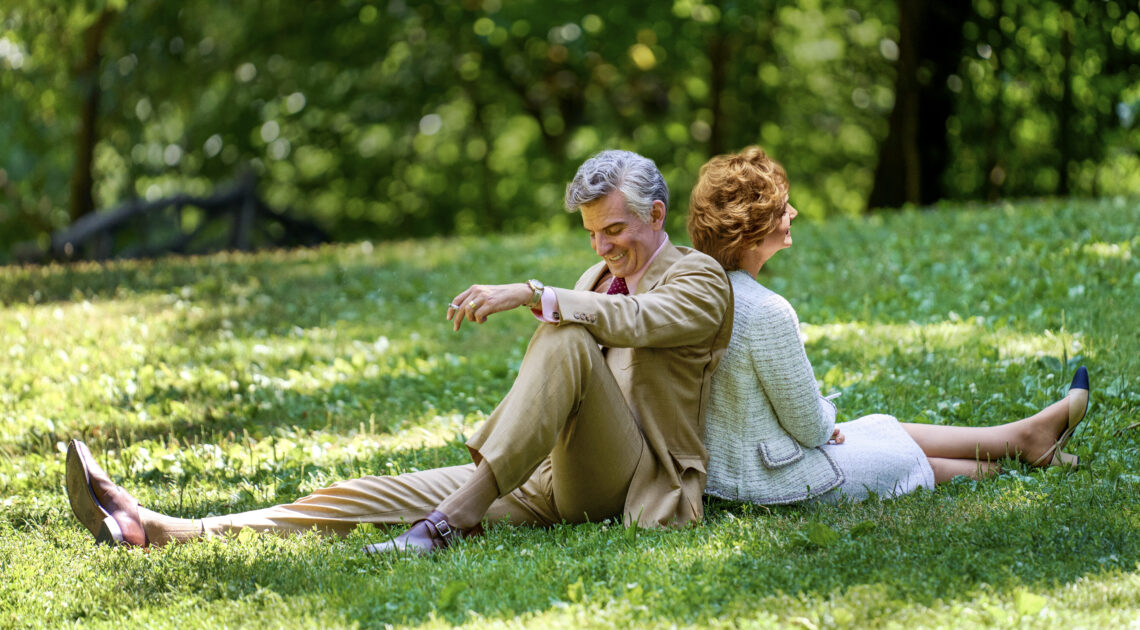 Szene aus dem Film Maestro. Ein MAnn und eine Frau sitzen Rücken and Rücken auf einer Wiese und lächeln