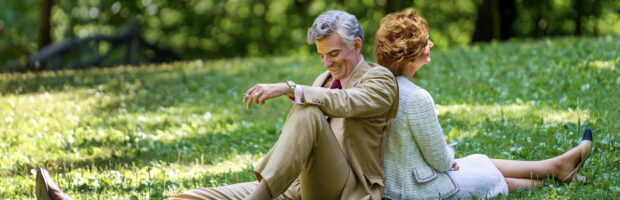 Szene aus dem Film Maestro. Ein MAnn und eine Frau sitzen Rücken and Rücken auf einer Wiese und lächeln