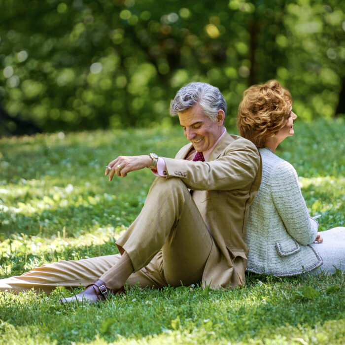 Szene aus dem Film Maestro. Ein MAnn und eine Frau sitzen Rücken and Rücken auf einer Wiese und lächeln