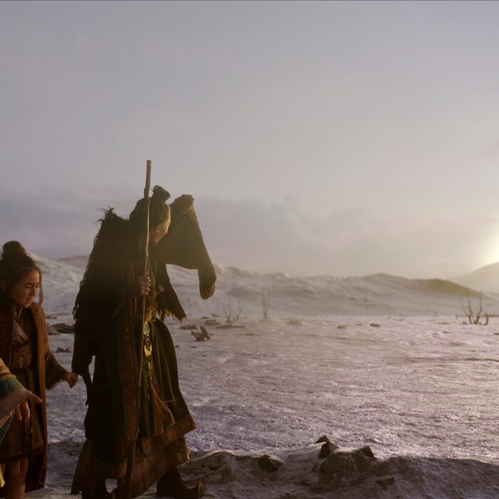 Szene aus der Serie. Man sieht drei Personen in traditionellen asiatischen Gewändern in einer kargen Landschaft stehen. Zwei halten ihre Hände vor ihr Gesicht, da am Horizont eine gleißend helle Kugel erscheint