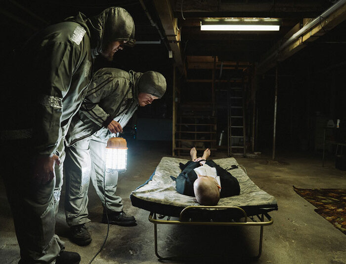 Szene aus dem Film Bugonia: Zwei Männer in silbernen Schutzanzügen beugen sich über eine Frau in Business Kleidung, die auf einer Liege in einem dunklen Keller liegt. Copyright Universal Pictures 2025