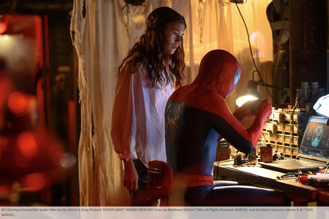Auszug aus dem Film Spider-Man Brand New Day. Spider-Man sitzt an einem Schreibtisch und bastelt etwas während MJ, gespielt von Zendaya, neben ihm steht und ihm hilfreiche Tipps gibt