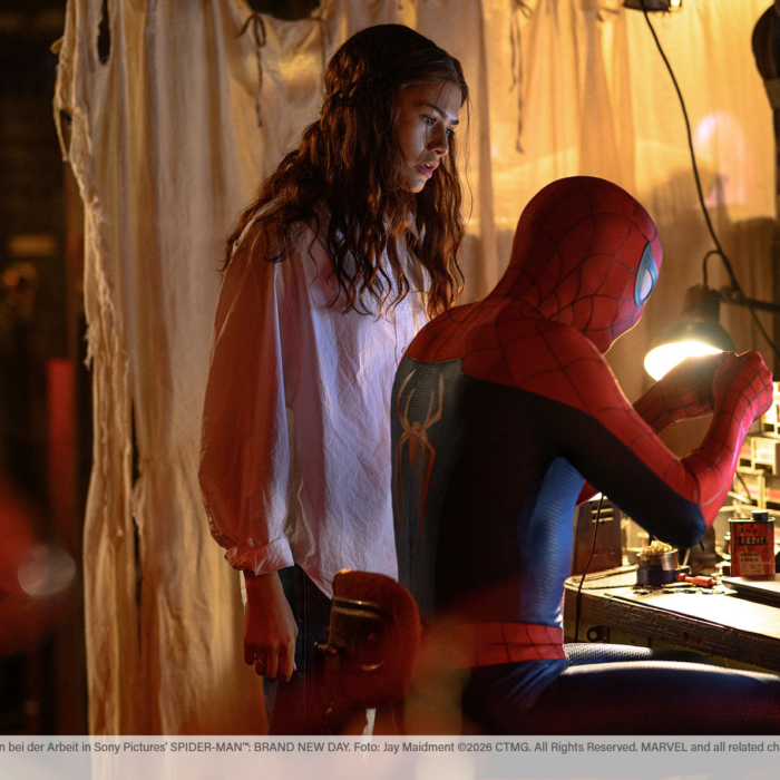 Auszug aus dem Film Spider-Man Brand New Day. Spider-Man sitzt an einem Schreibtisch und bastelt etwas während MJ, gespielt von Zendaya, neben ihm steht und ihm hilfreiche Tipps gibt